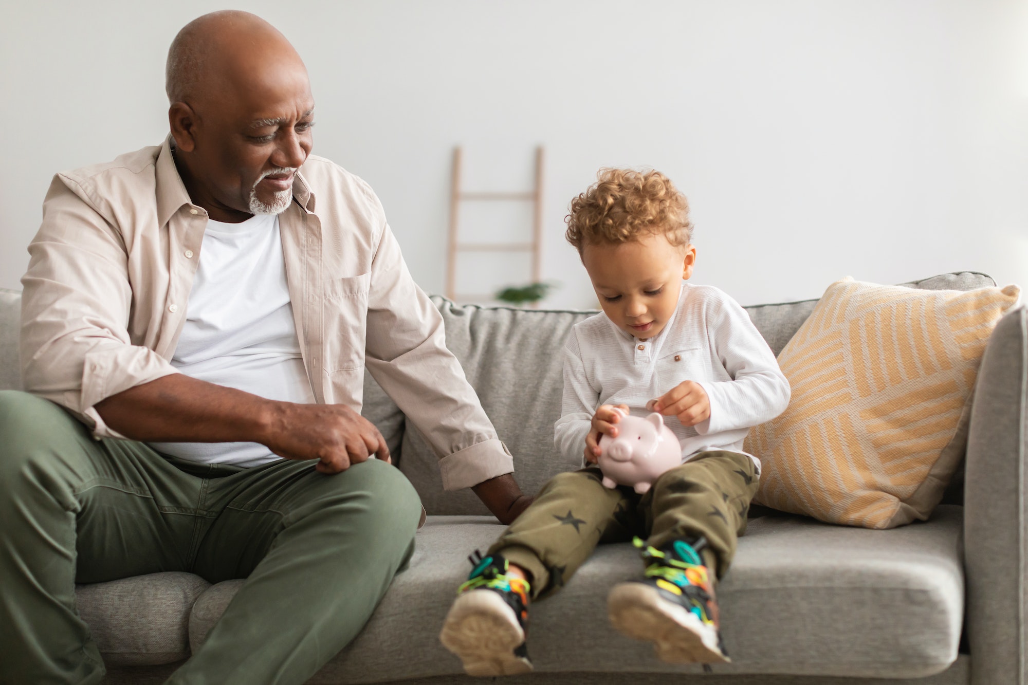 African American Grandpa And Grandson Putting Money In Piggybank Indoor