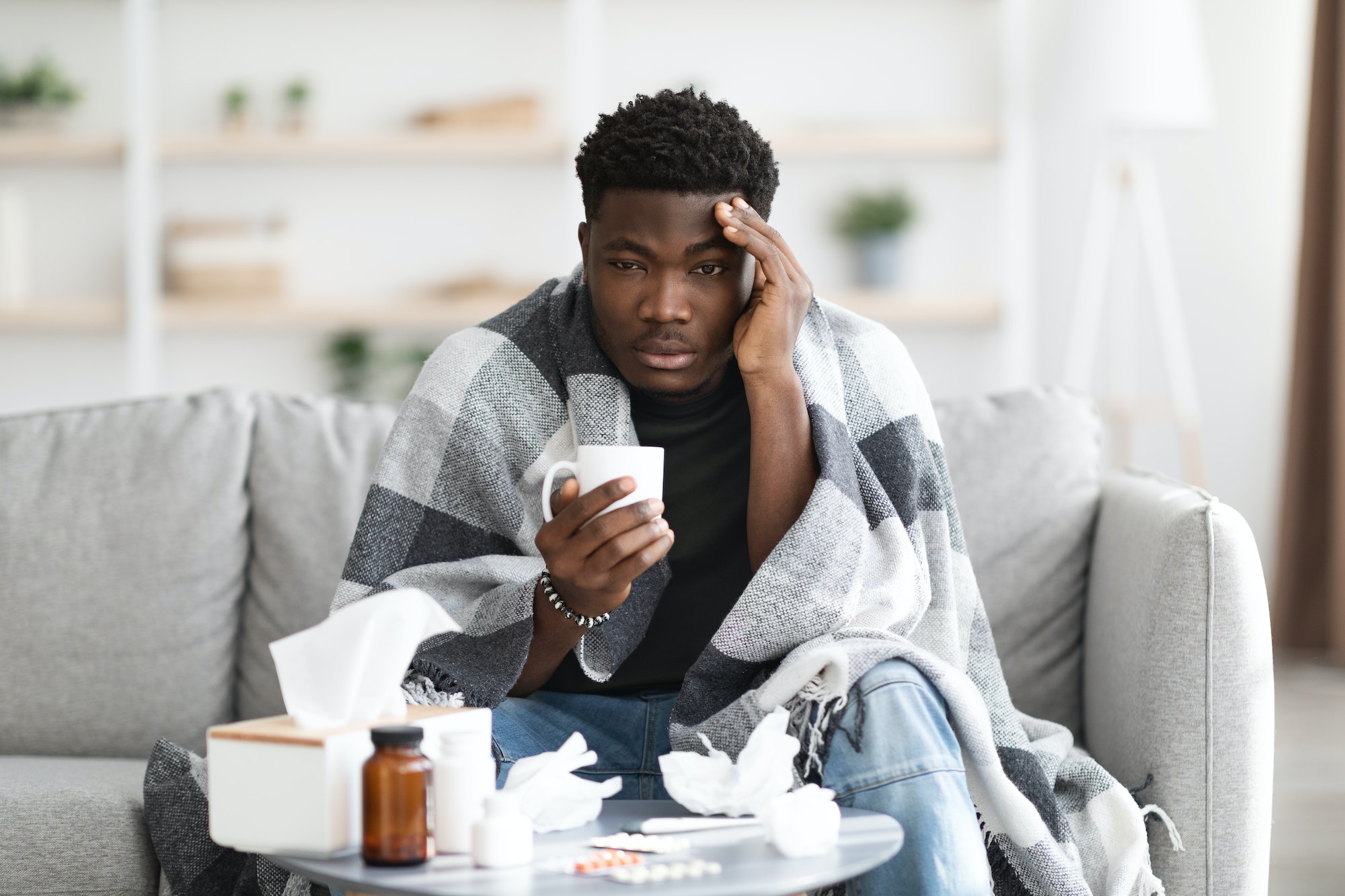 Upset black man having flu, drinking warm tea