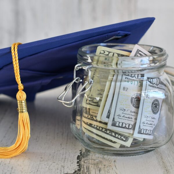 Making College More Affordable - Graduation cap mortarboard with tassel propped on a jar of money cash, concept school loans debt