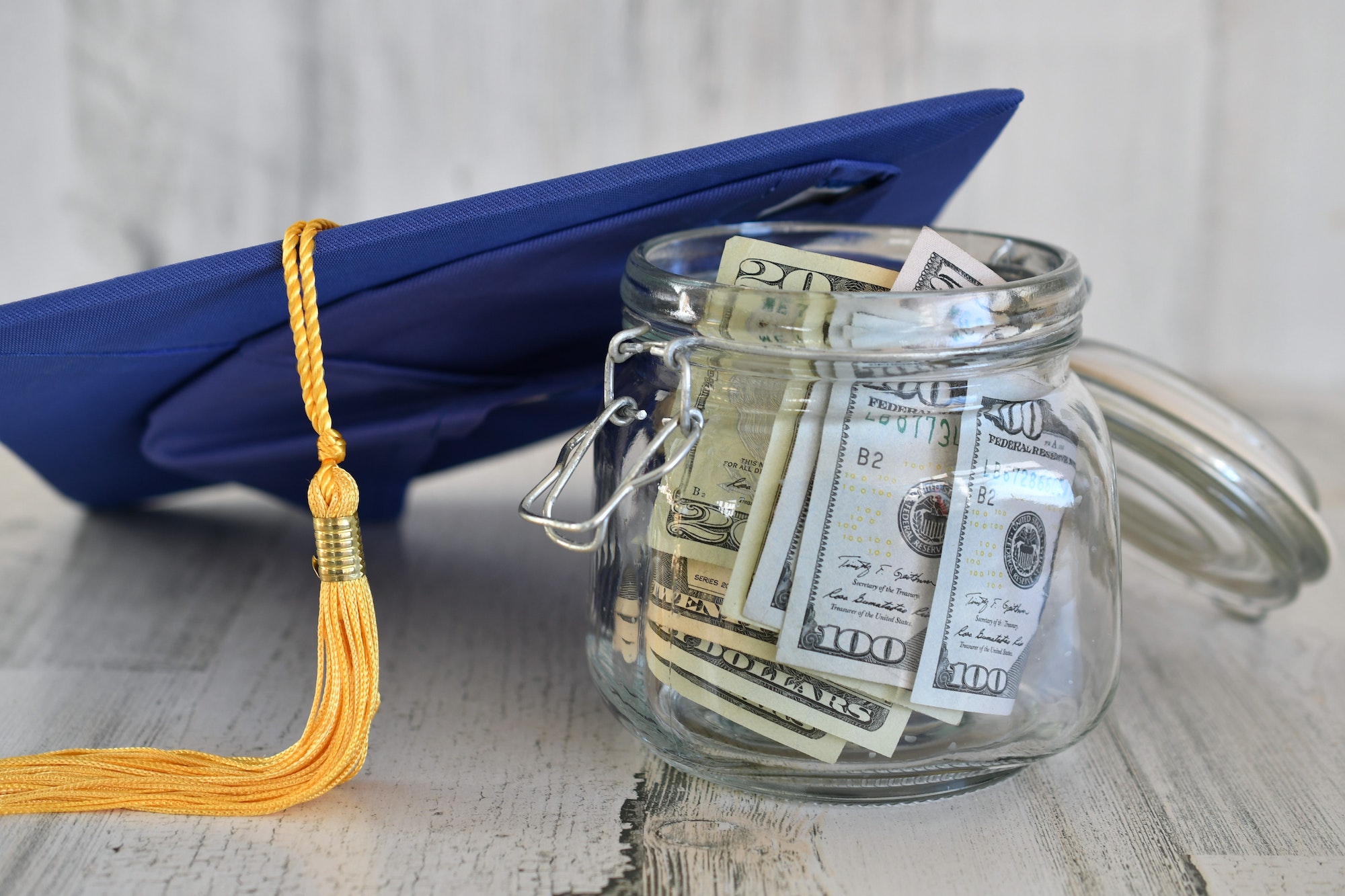 Making College More Affordable - Graduation cap mortarboard with tassel propped on a jar of money cash, concept school loans debt